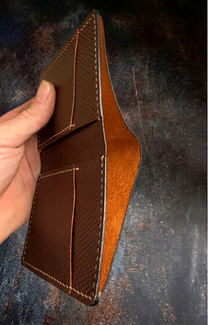 Brown leather wallet held by a hand against a dark textured background