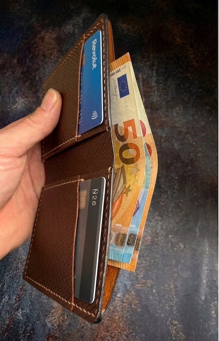 Hand holding a brown leather wallet with cards and money on a dark textured background